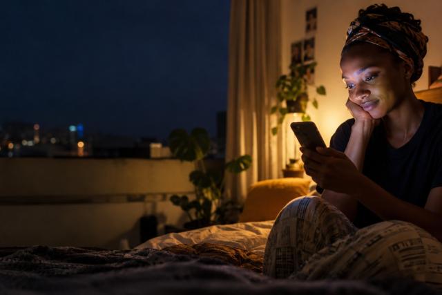 Young African woman using her smartphone at night, illustrating the growing use of AI chatbots for mental health support.